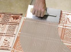 Using a trowel the glue is applied to the back of the metal backsplash tiles.