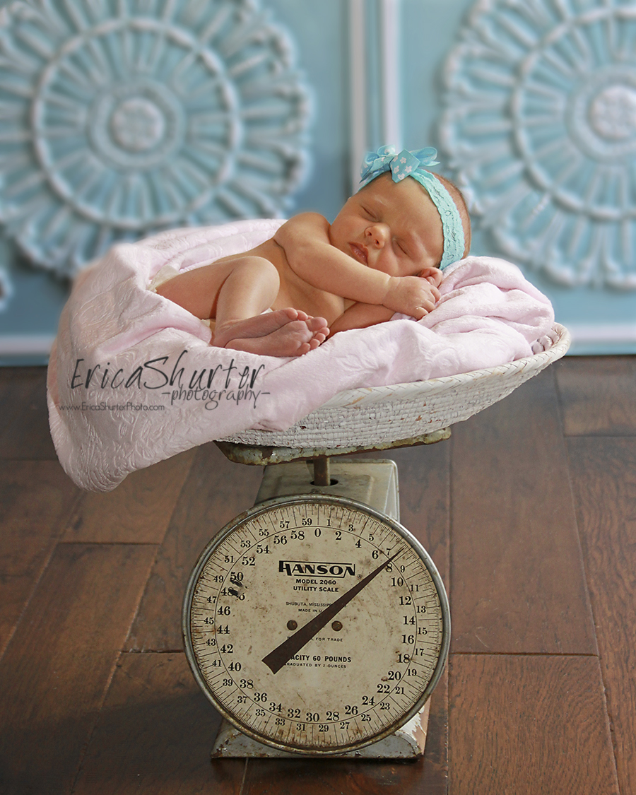 Sleeping baby on in the blanket on top of a vintage scale with blue photography backdrops.